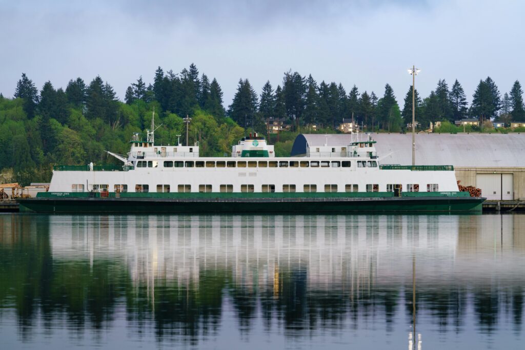 a ferry moored in a tranquil harbor surrounded by lush trees, reflecting on calm waters.