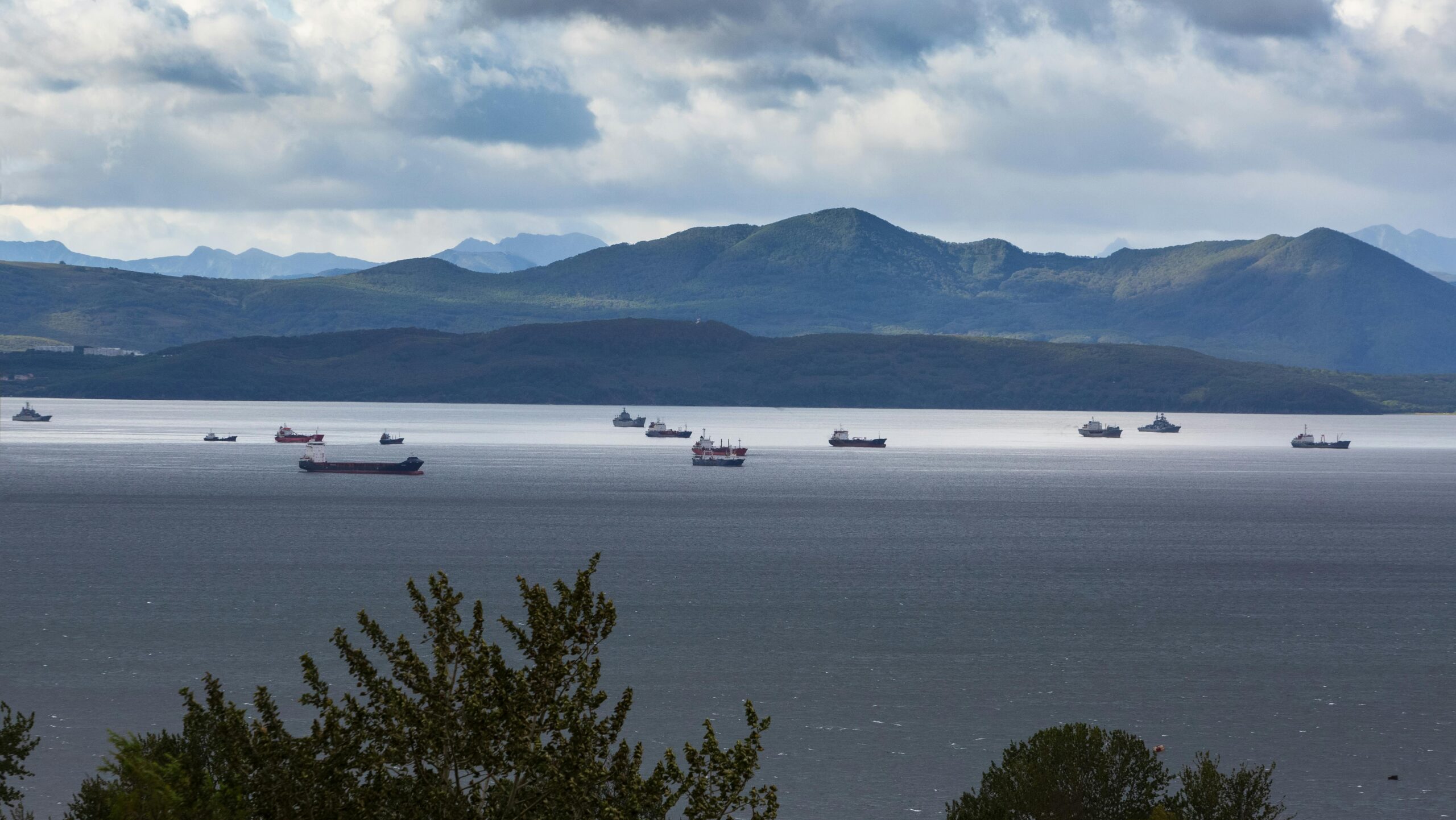 scenic view of ships on a calm sea against a mountainous backdrop under cloudy skies.