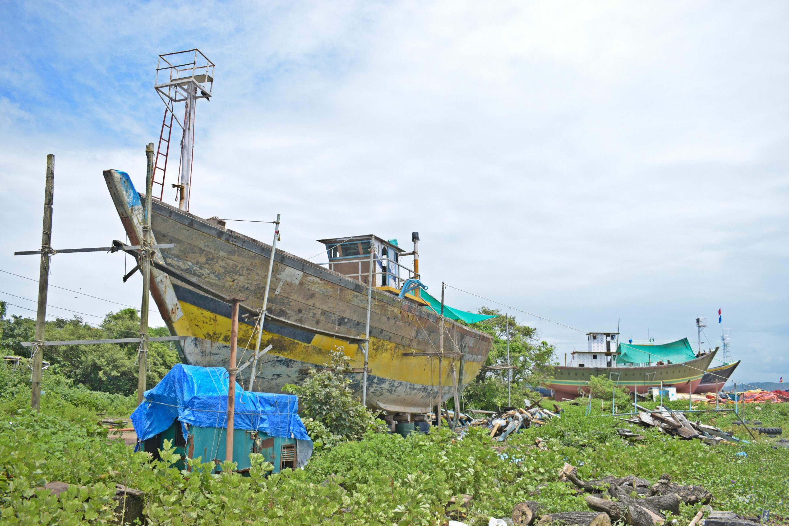 weathered and abandoned ships on a coast surrounded by greenery under a cloudy sky.