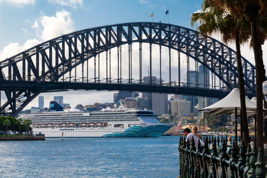 a bustling view of a cruise ship passing under the iconic sydney harbour bridge in australia.