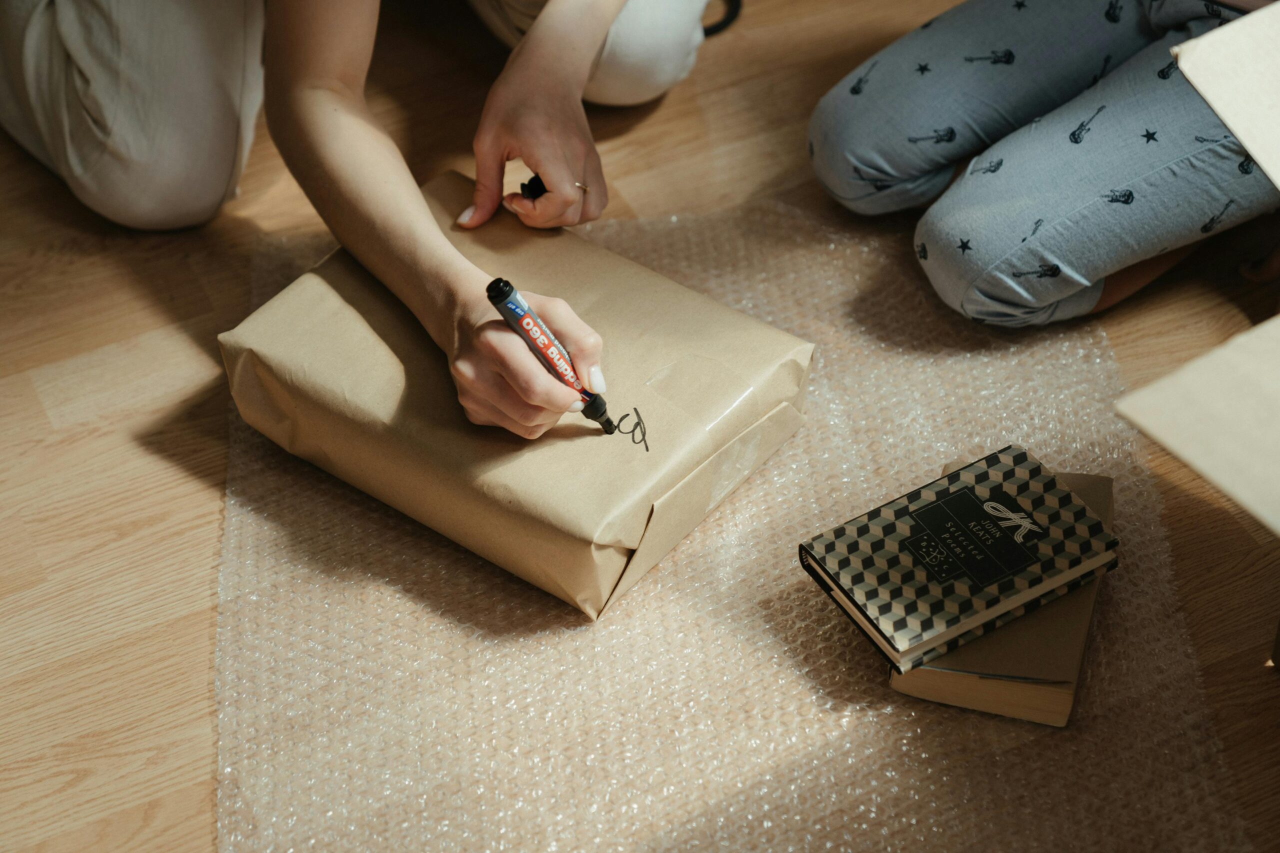 hands writing on a wrapped package, preparing books with bubble wrap for secure shipping.