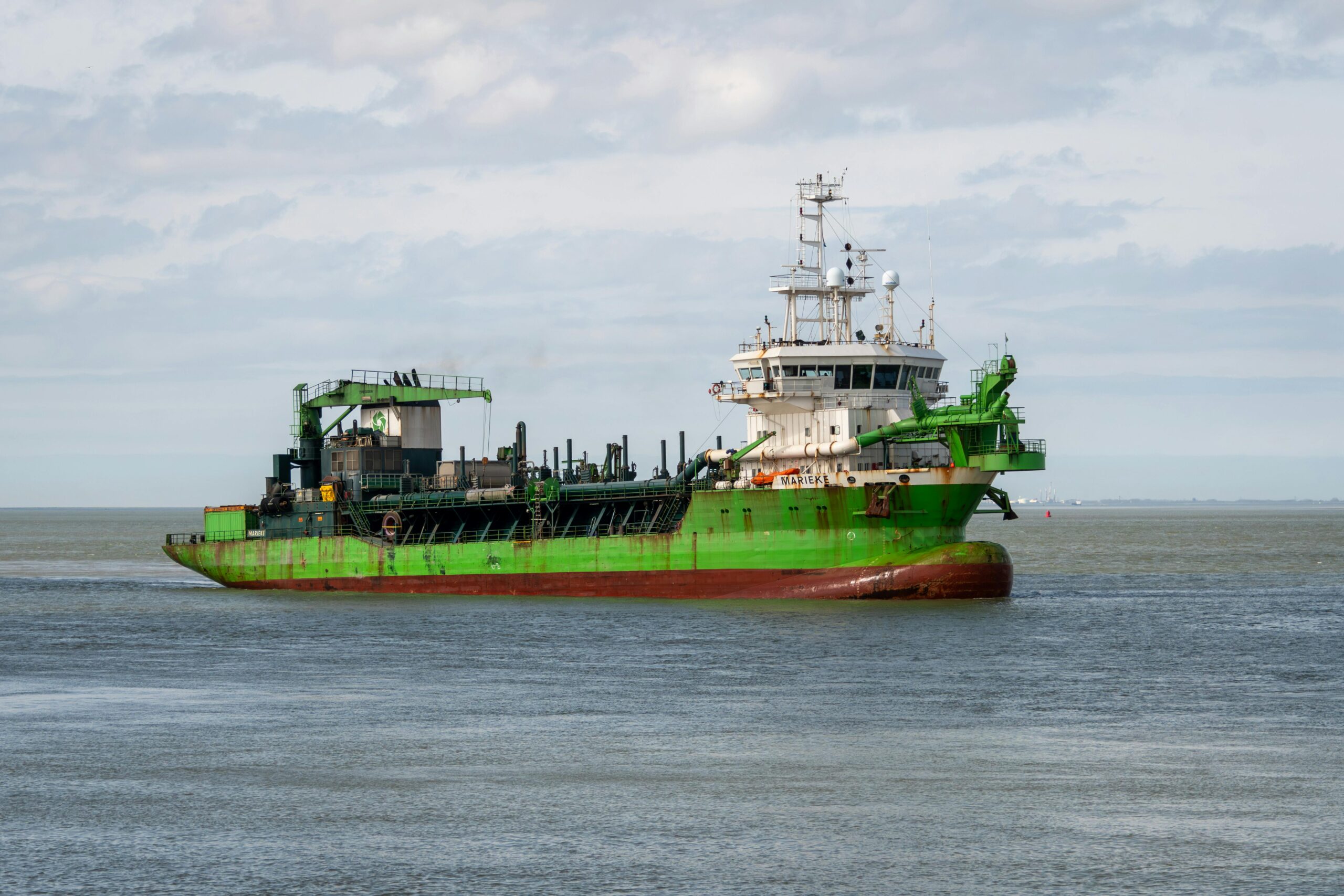 large green cargo ship sailing on calm ocean waters under a cloudy sky.