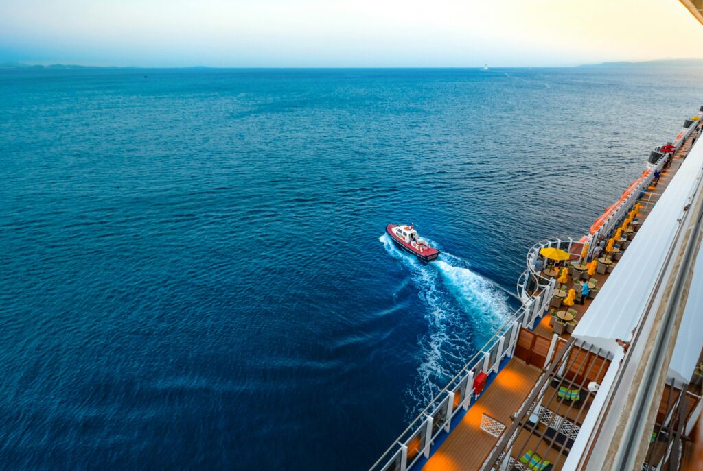 aerial view of a luxury cruise ship with a small boat on a vast ocean at sunset.