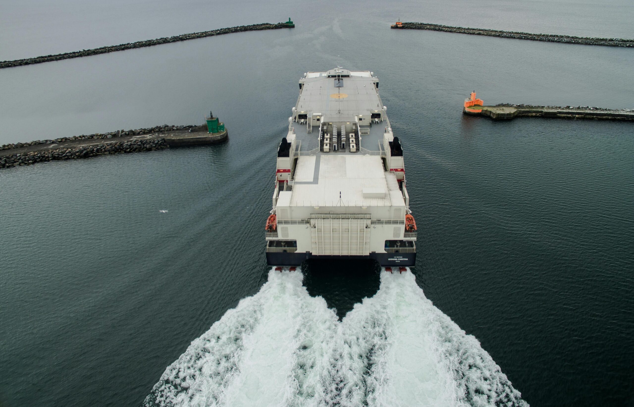 aerial view of a ferry leaving the harbor between breakwaters, showcasing transportation on the sea.