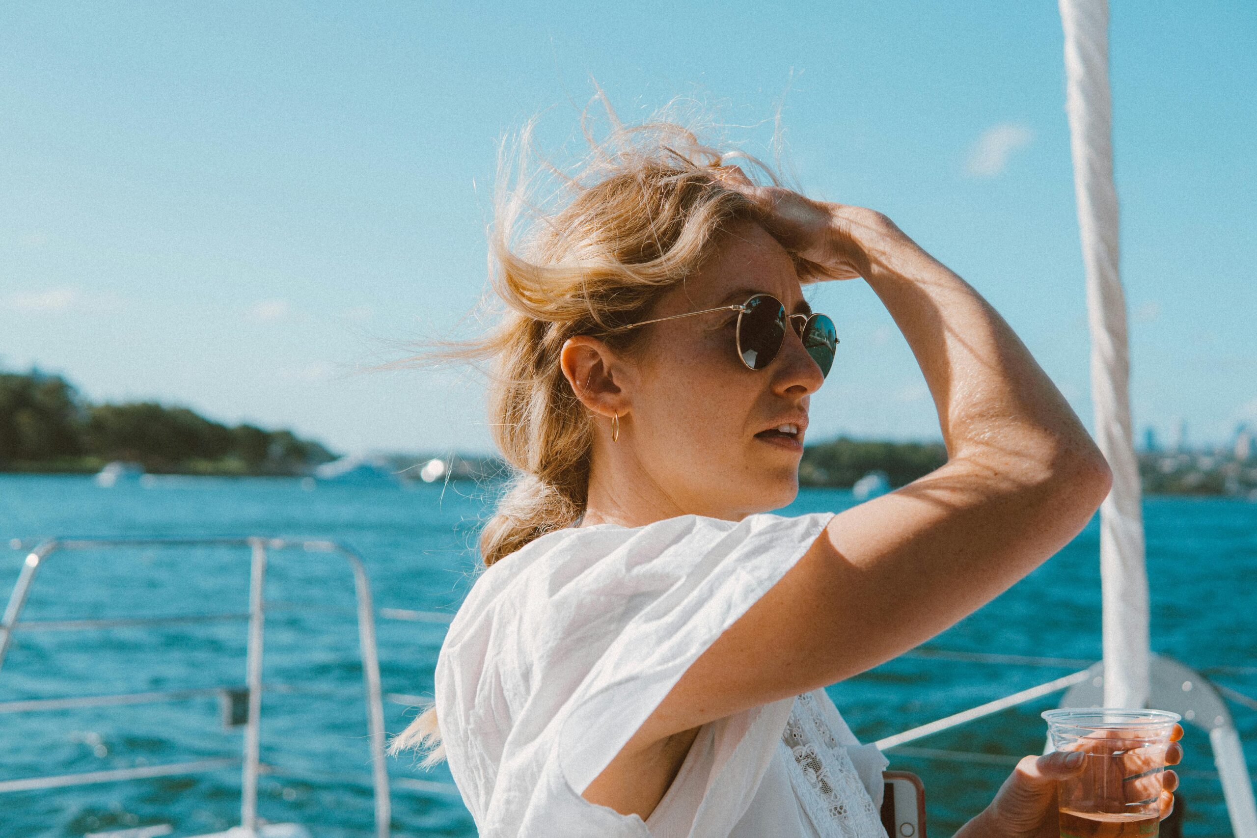 a woman on a yacht enjoying a sunny day at sea, sporting sunglasses and a relaxed demeanor.