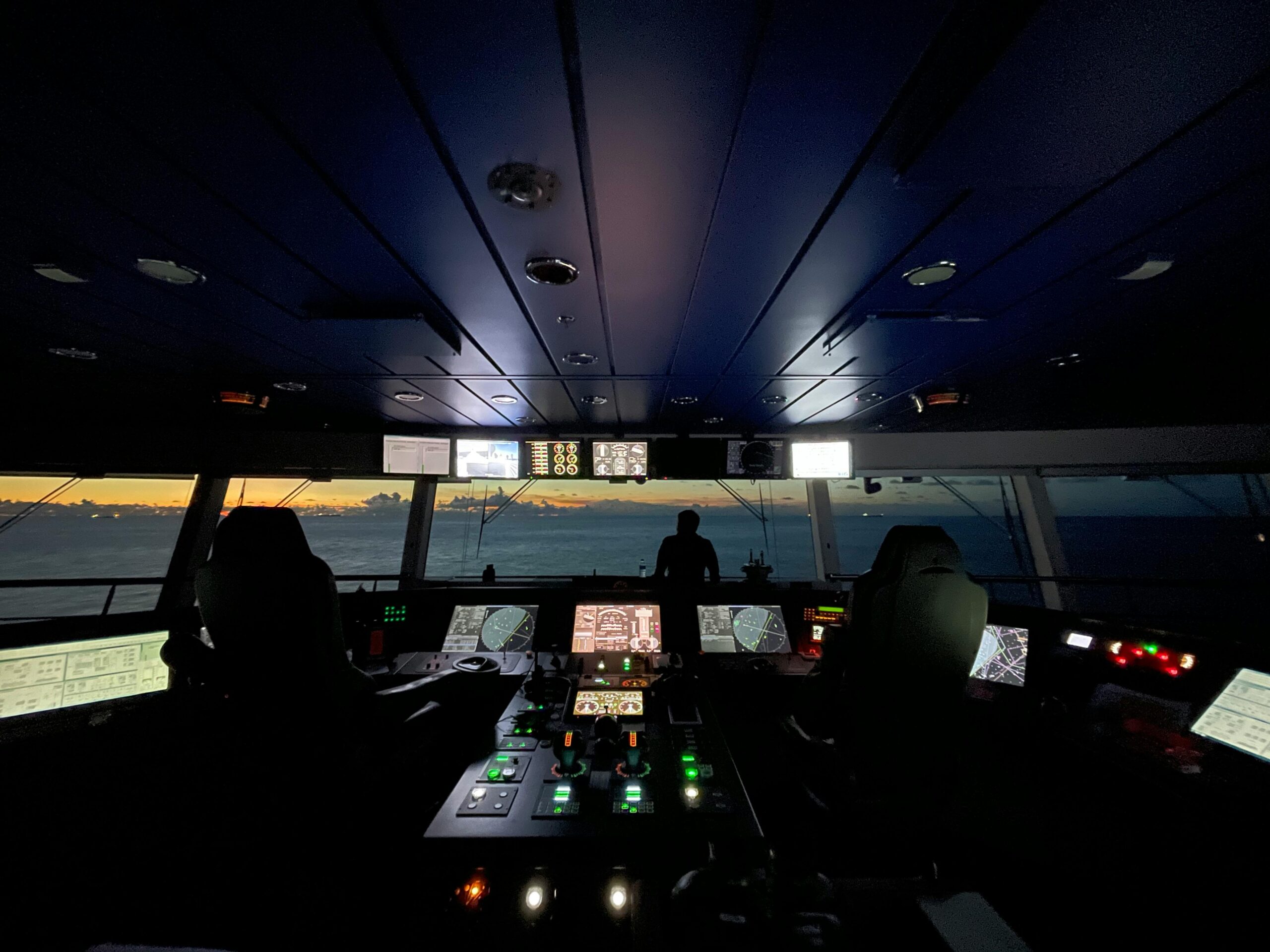 person silhouettes in a ship's control room viewing ocean sunrise