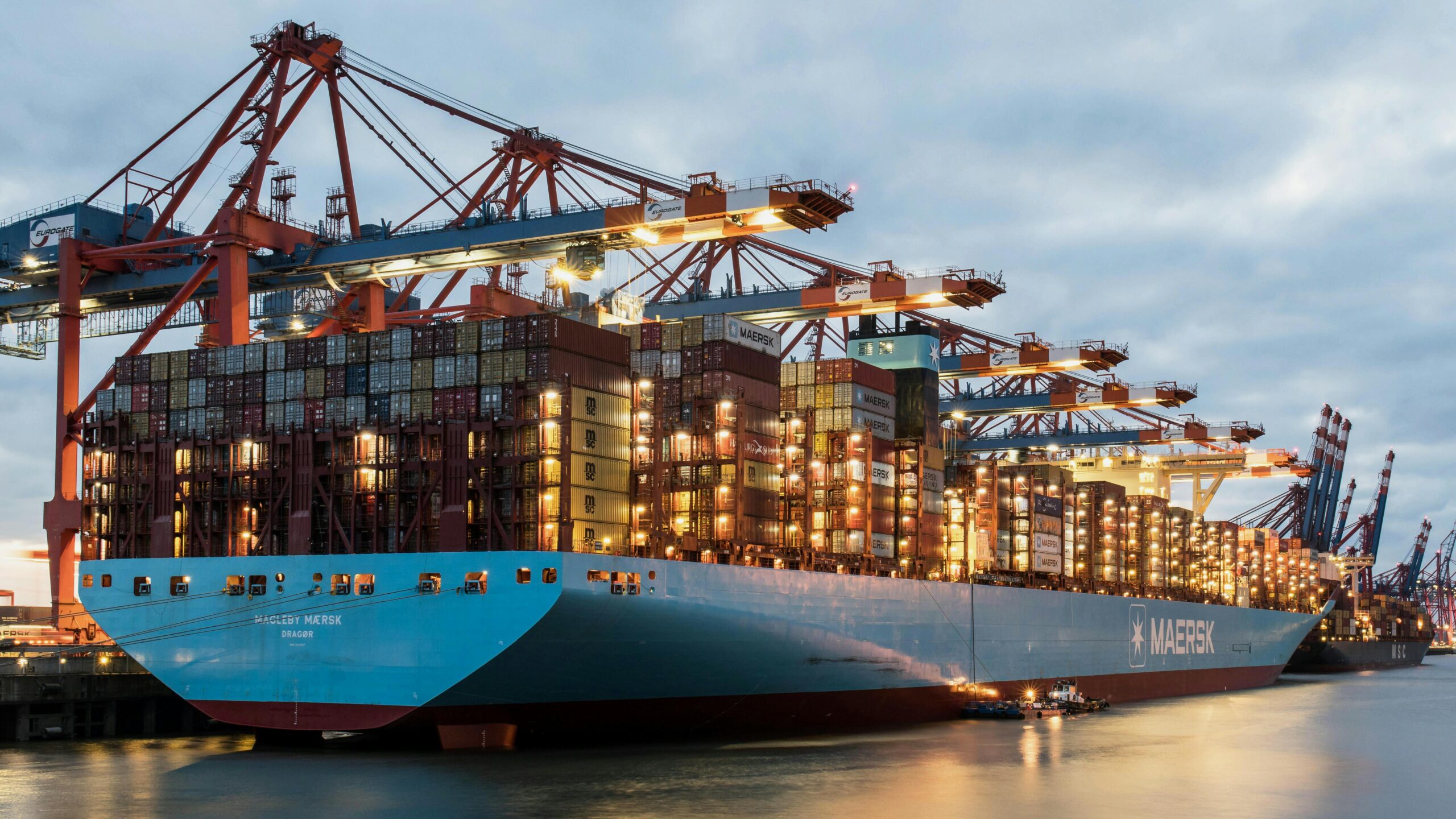 view of a large cargo ship being loaded at hamburg harbor during twilight.