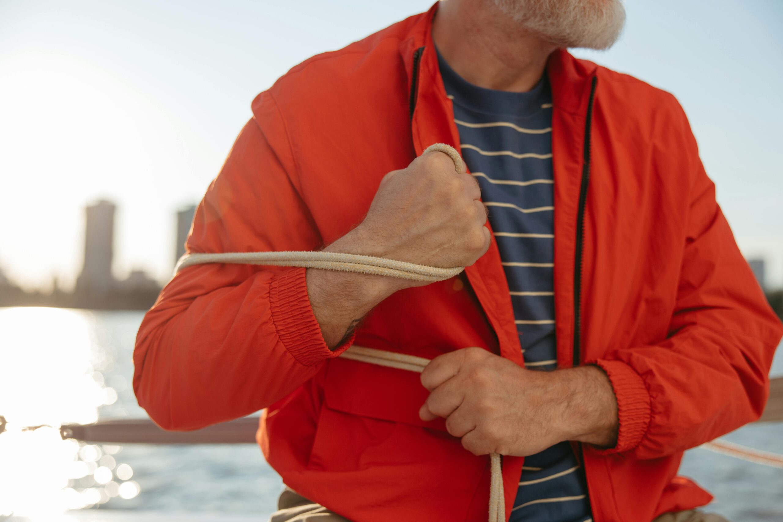 a man in an orange jacket holding a rope, hinting at maritime activity on a sunny day.