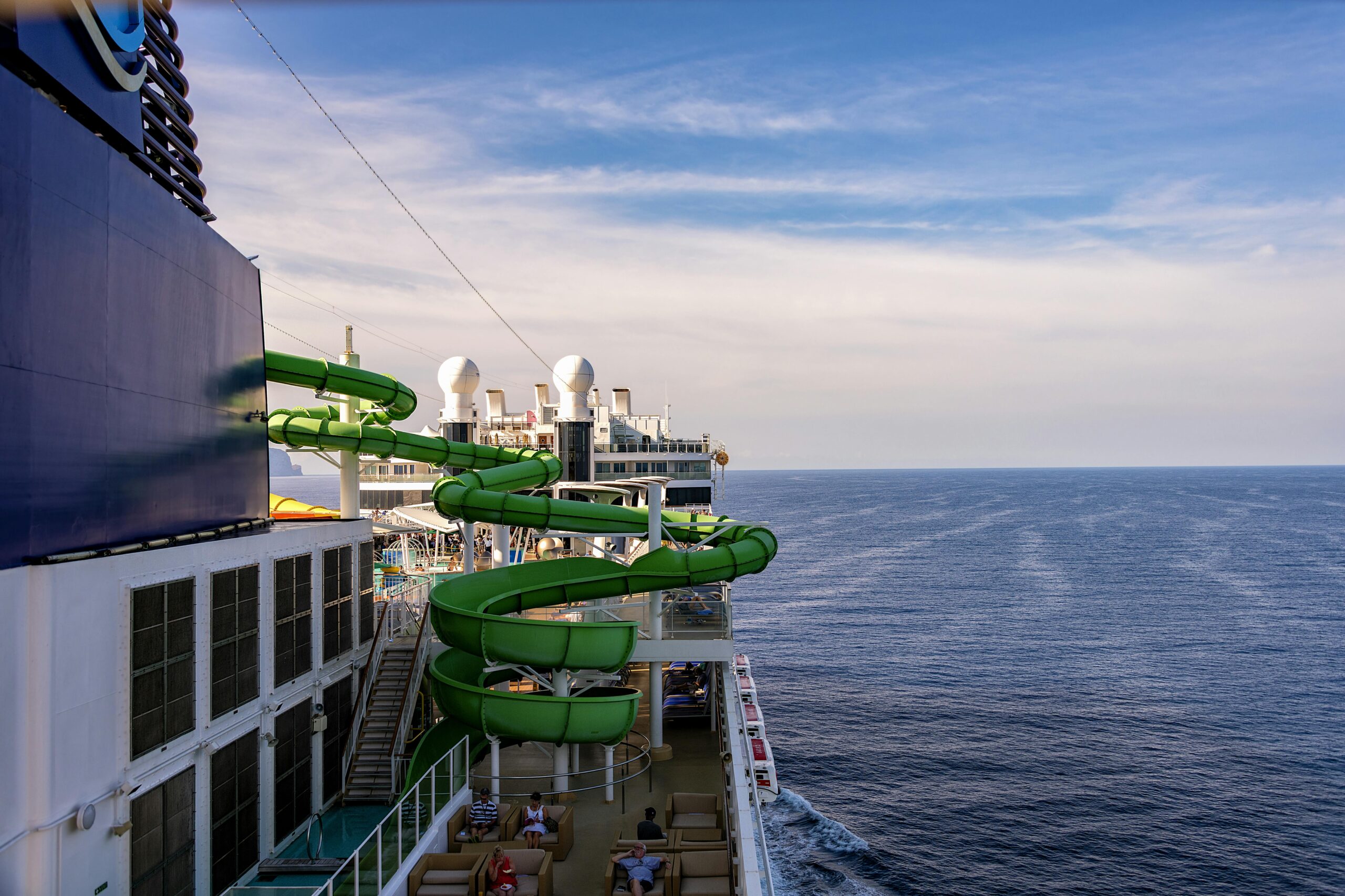 cruise ship featuring a vibrant green waterslide sailing through the open sea under a clear sky.
