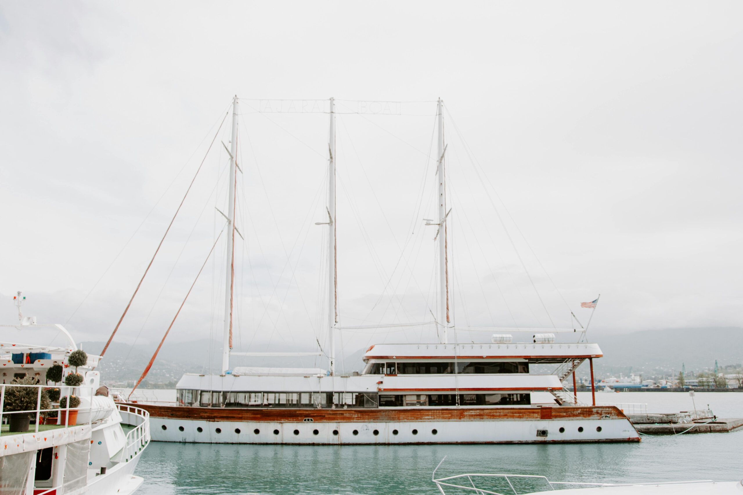elegant sailing yacht anchored at a serene port with mountains in the background.