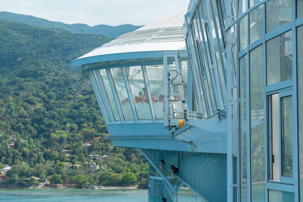 a modern cruise ship deck with glass enclosure overlooking a lush coastal landscape.
