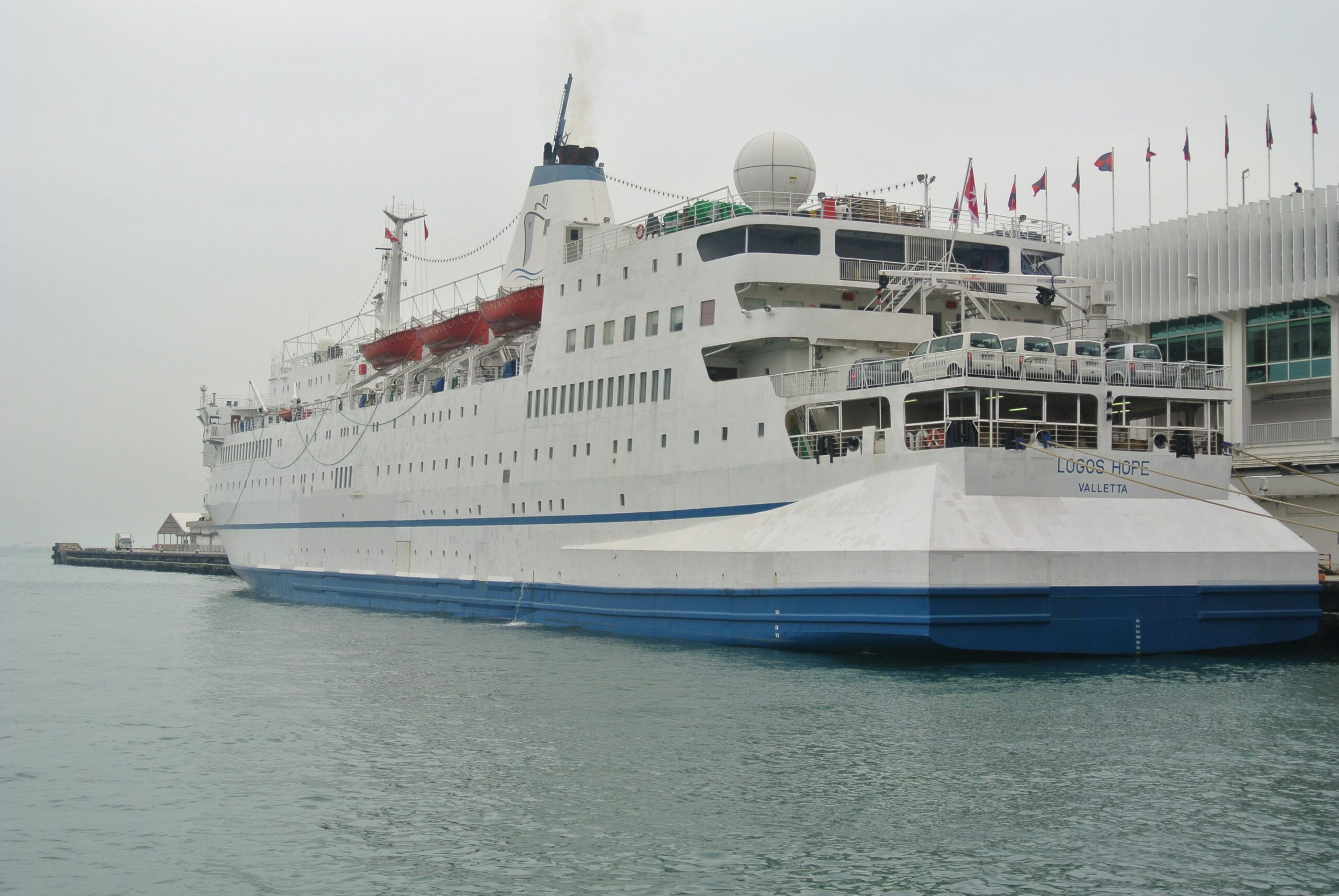 a large ferry ship docked at a passenger terminal in hong kong, featuring white and blue colors.