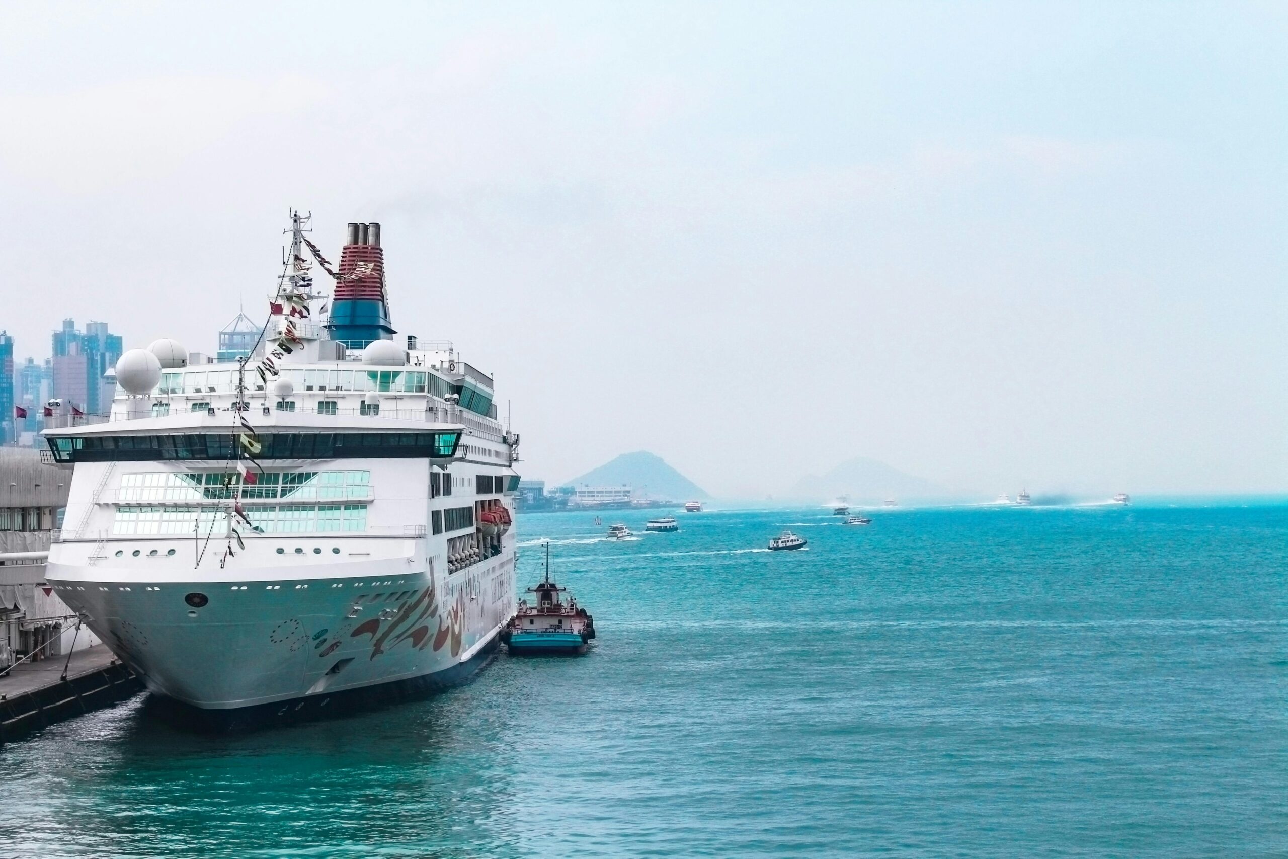a luxury cruise ship docked at a bustling harbor with clear blue waters and city skyline backdrop.
