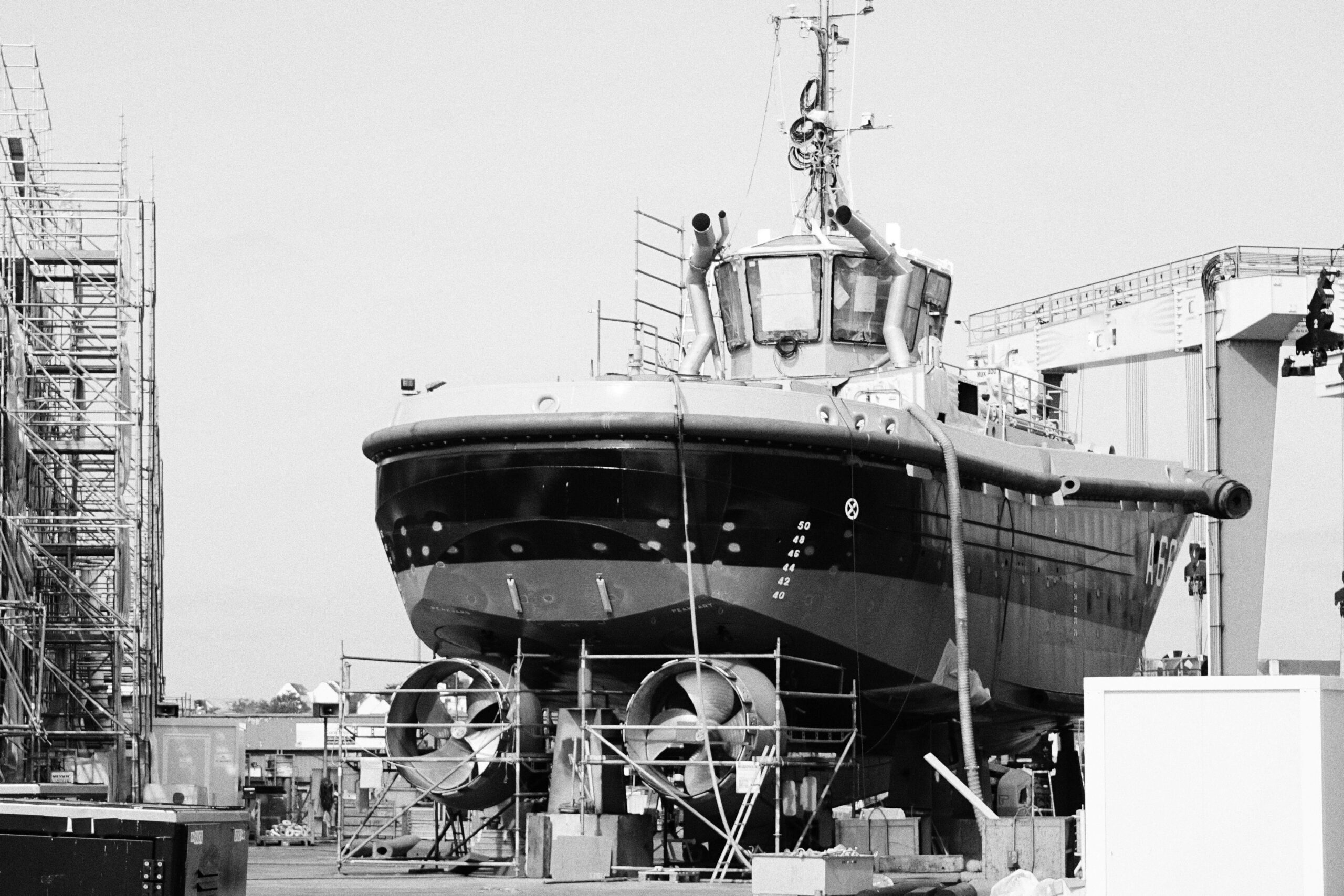 black and white image of a vessel in a shipyard, showcasing industrial shipbuilding infrastructure.