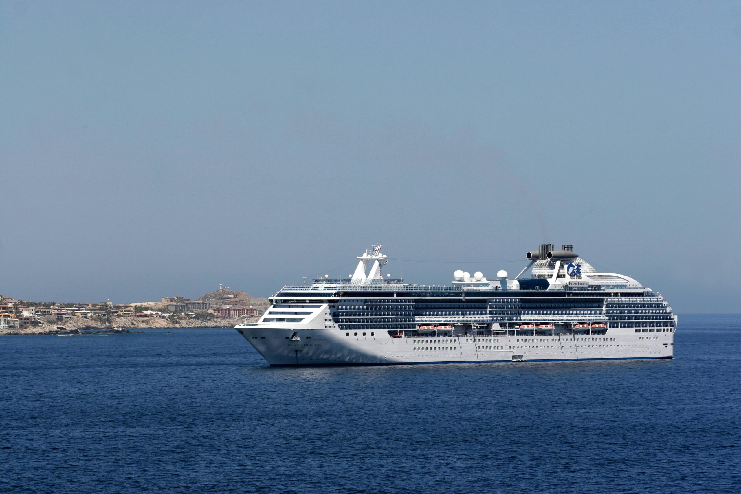 a large cruise ship sailing on the ocean near a scenic coastline under a clear blue sky.