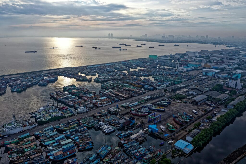 discover jakarta's harbor at sunrise, showcasing boats, industrial buildings, and cityscape.