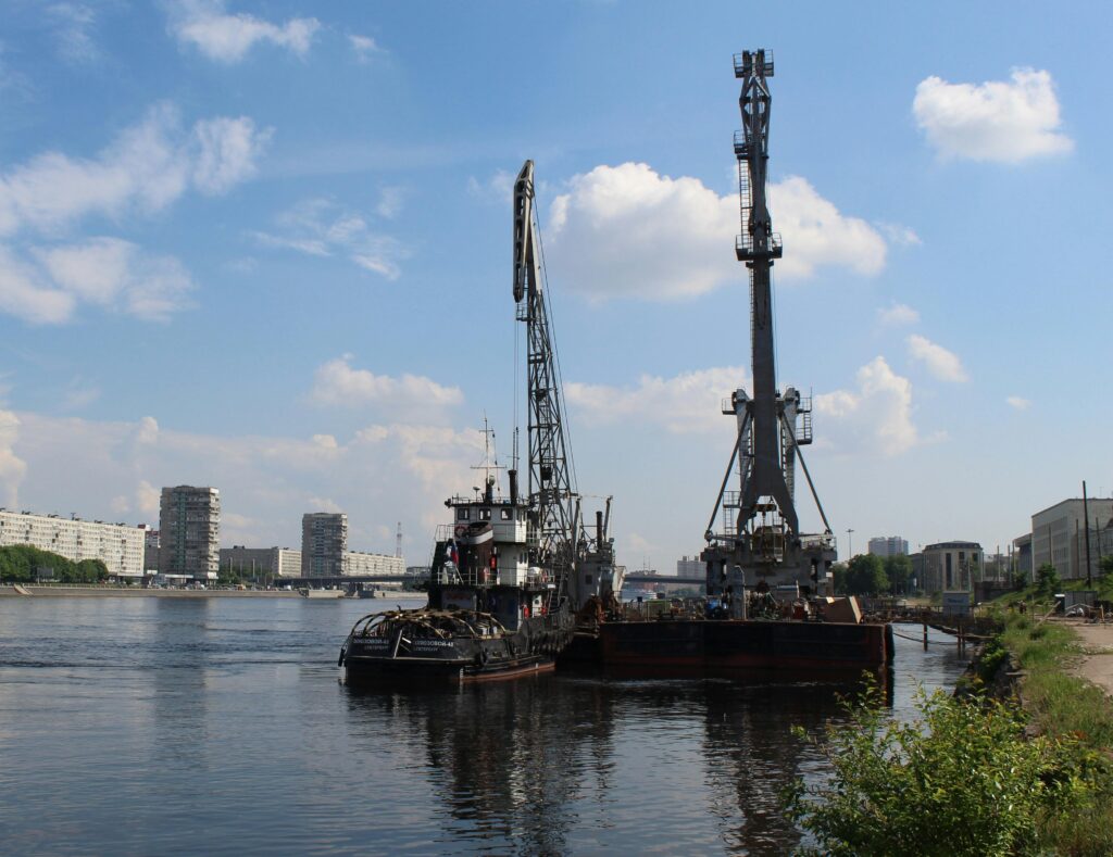 a bustling industrial harbor with cranes loading ships under a sunny summer sky.