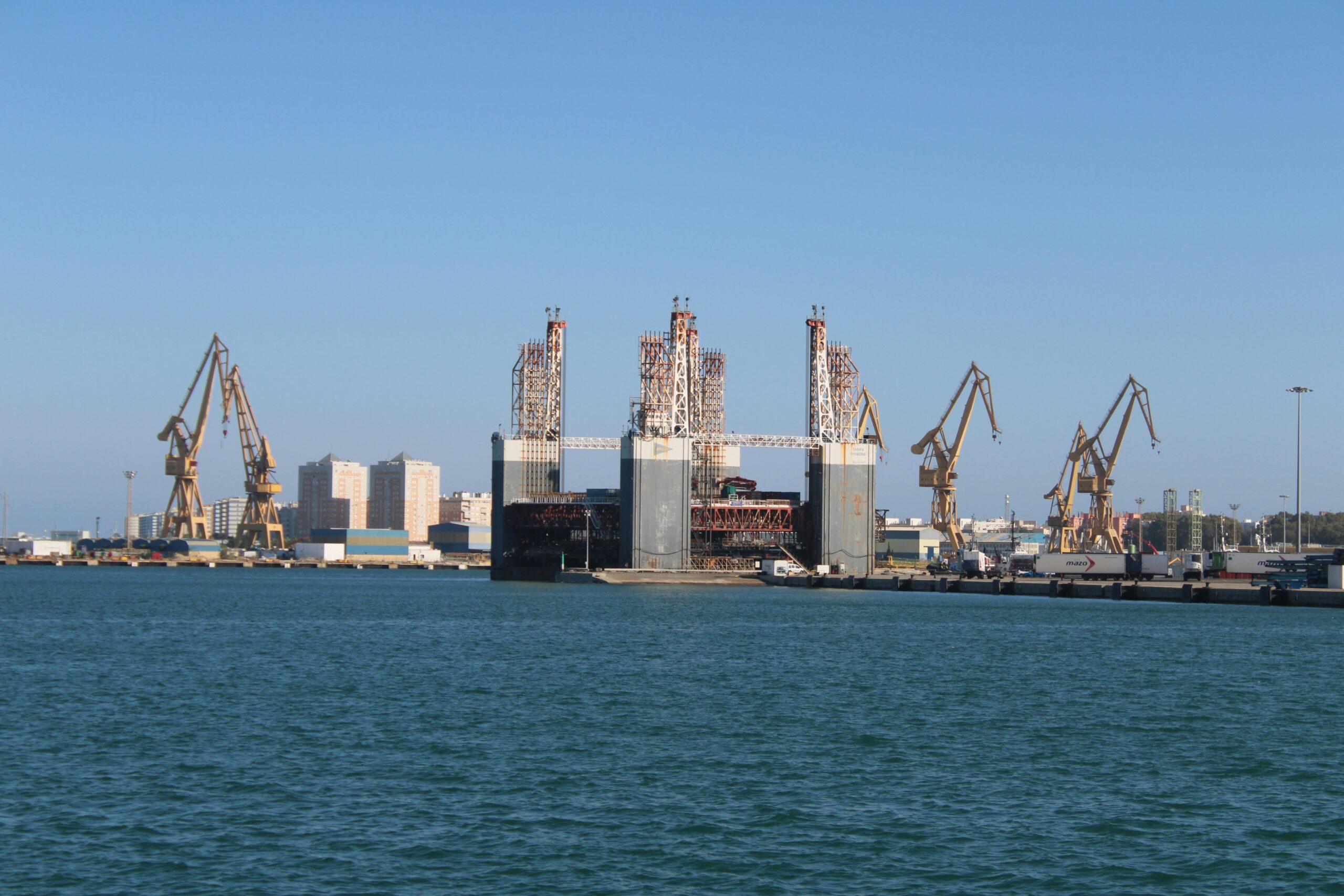 a panoramic view of cádiz harbor featuring industrial cranes and a city skyline.