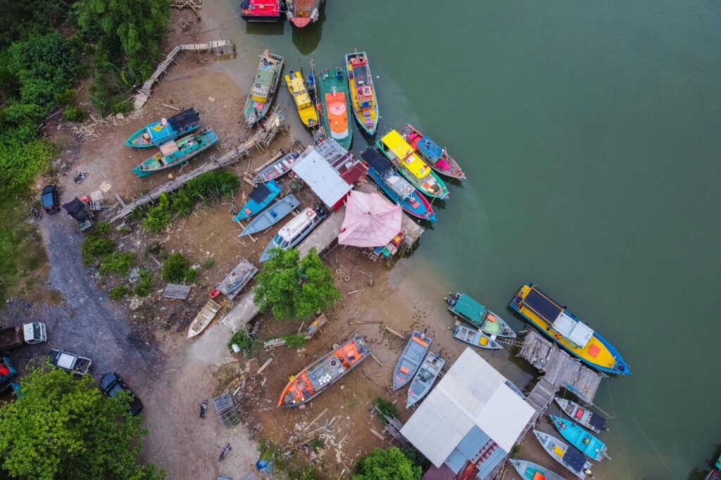 aerial shot of vibrant boats docked at a riverside in chukai, malaysia with lush greenery.