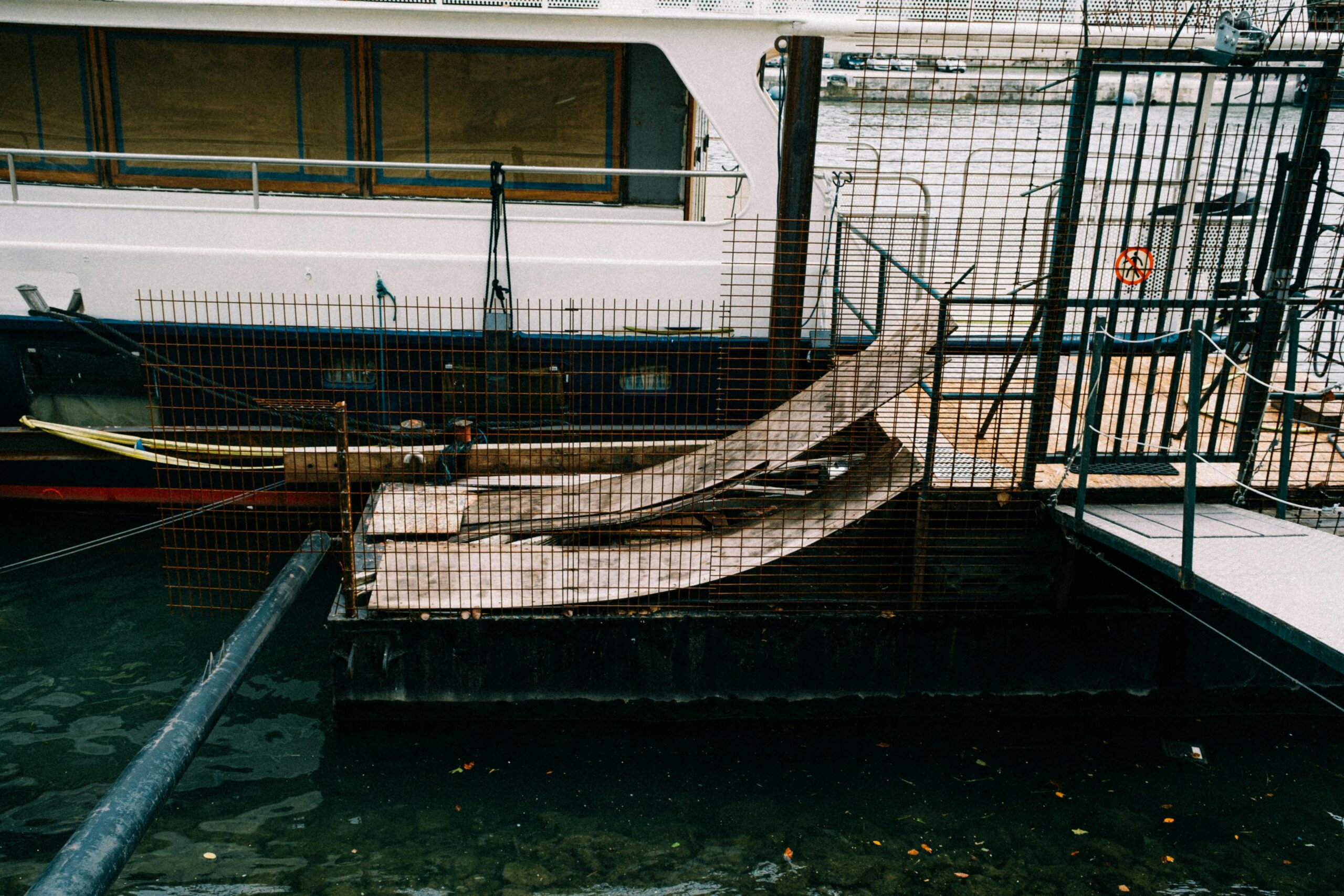 a boat moored at a dockside in an industrial setting, featuring metal railings and ramps.